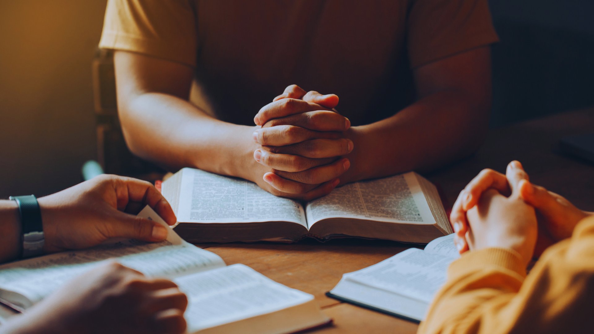 Hands joined in prayer over open Bibles
